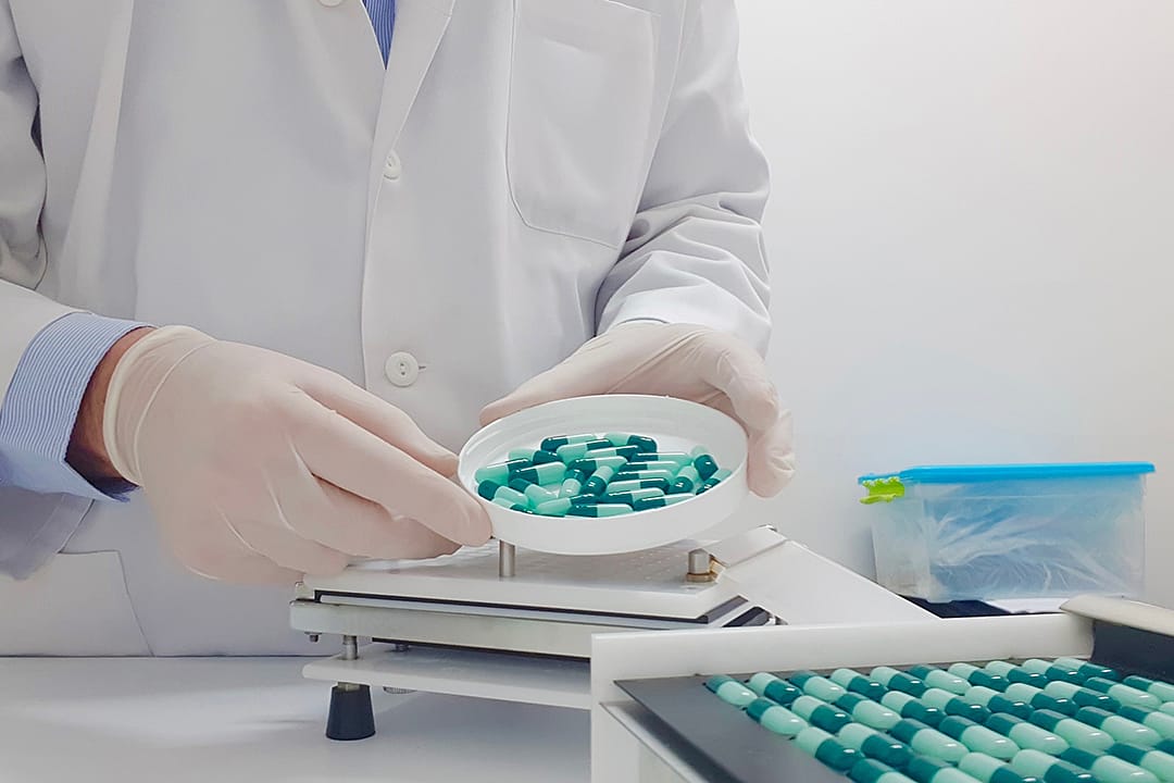 A specialized pharmacist using a manual filling machine to compound medicine capsules in a laboratory.